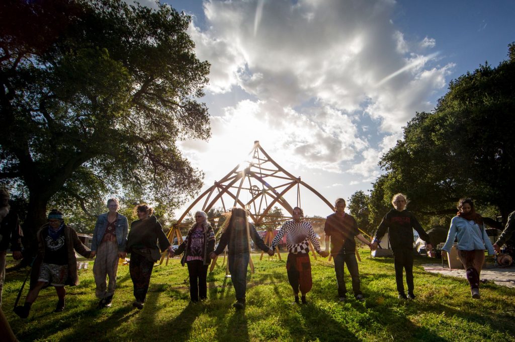 Nine diverse people of different ages and ethnicity joined in hands spanning across field walking forward