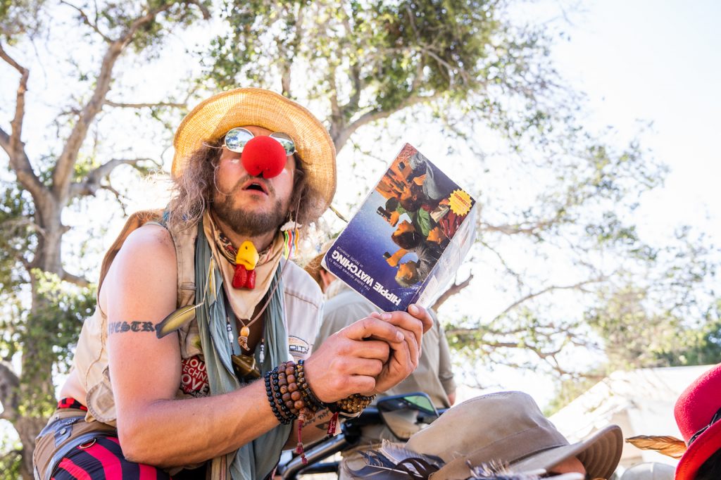 Clown-nosed man holding upside down pamphlet titled: Hippie Watching.